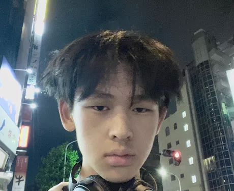 A young man in a city with headphones around his neck looks directly at the camera