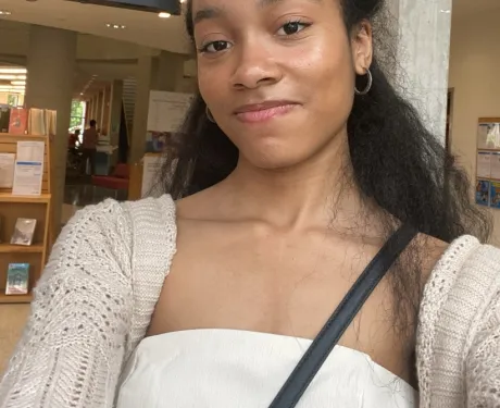 A selfie of a teenage girl with long hair pulled half back, wearing a white shirt and beige cardigan. 