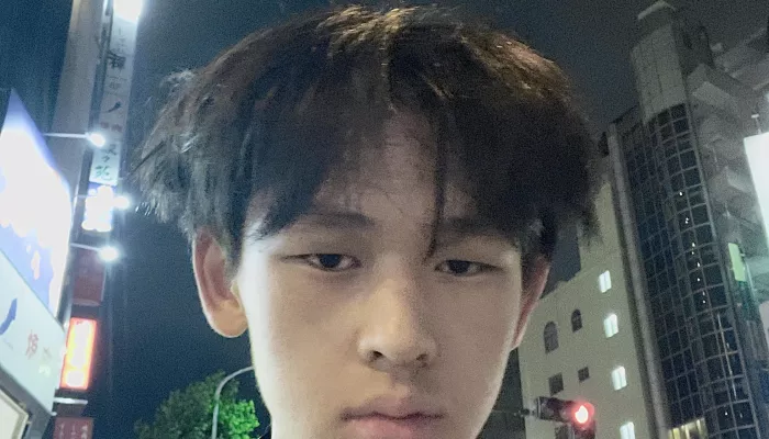 A young man in a city with headphones around his neck looks directly at the camera